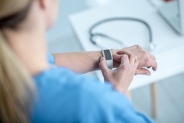 A close-up of a smartwatch displaying a patient's vital signs, with a doctor reviewing the data on a tablet. The focus is on the seamless integration of wearable technology with healthcare systems, representing real-time health monitoring and personalized feedback.