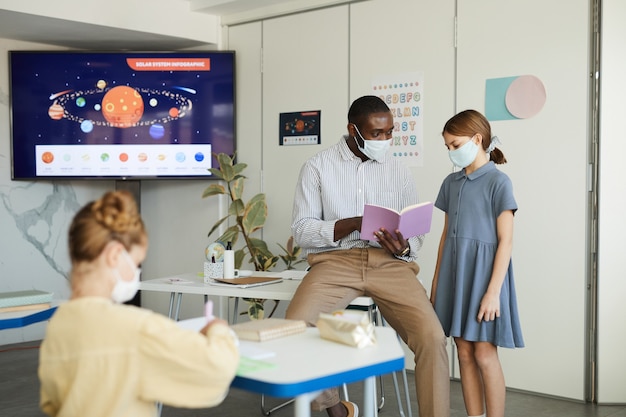 A teacher awarding a student a virtual badge on a digital platform, displayed on a large screen in the classroom. Other students are looking on with interest and excitement.