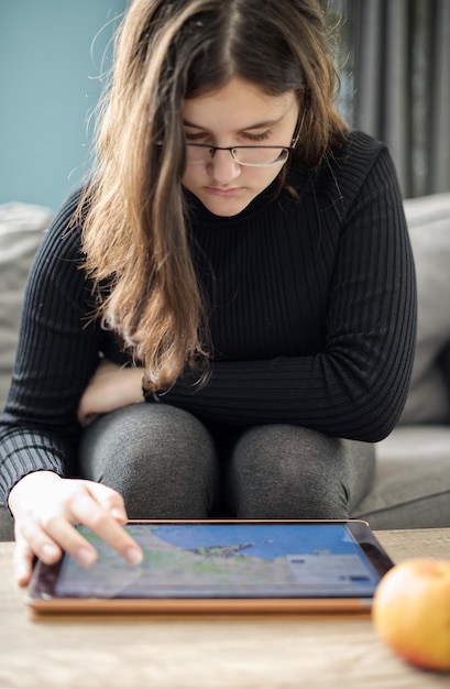 A student with a visual impairment using a tablet with a text-to-speech educational app. The student is wearing headphones and focusing on the screen. The app has adjustable font sizes and contrast settings.
