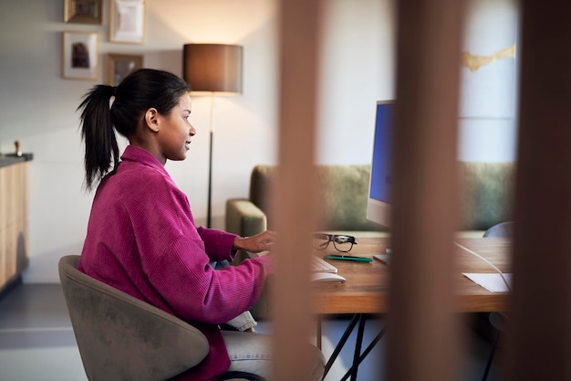 An employee working from home in a comfortable, brightly lit home office. They are participating in a video conference call with colleagues, smiling and engaged. The background shows a clean and organized workspace with natural light.