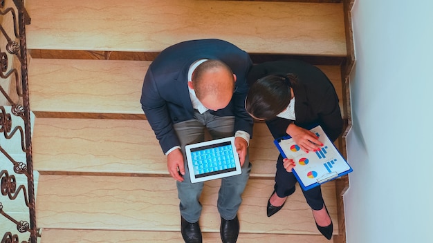 A split screen showing remote and in-office workers seamlessly collaborating on a project using digital tools. On one side, a person is working from home on a laptop, reviewing documents. On the other side, a team is gathered around a large interactive whiteboard, brainstorming ideas.